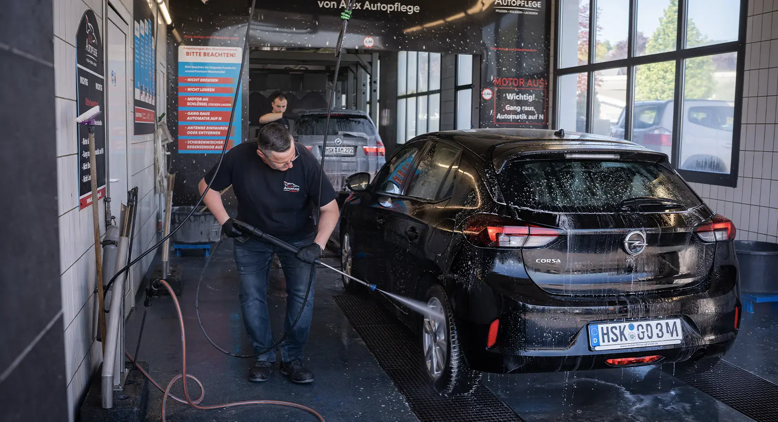 In der Waschstraße wird ein Auto von einem Mitarbeiter mit einem Hochdruckreiniger gereinigt